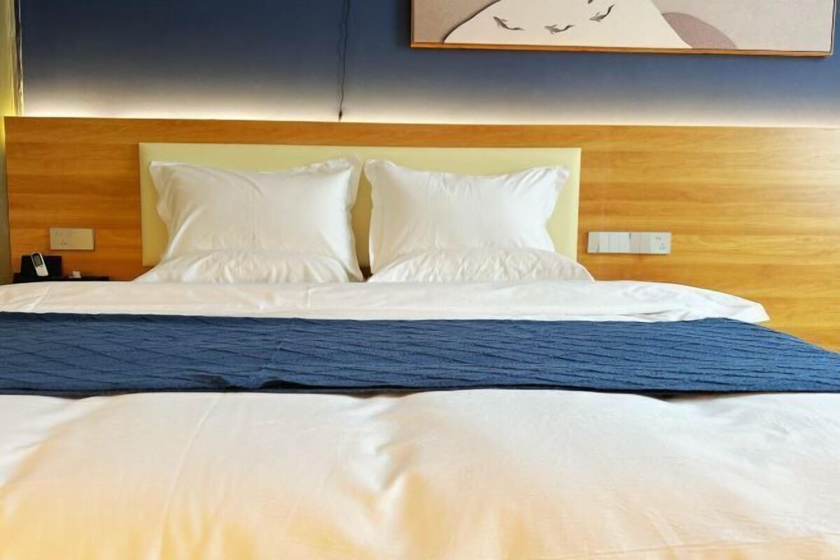 A hotel room with a large bed, two pillows, a wooden headboard, and a painting on the wall.