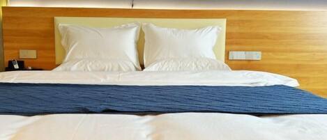 Un cuarto de hotel con una cama grande, dos almohadas, un cabecero de madera y un cuadro en la pared.