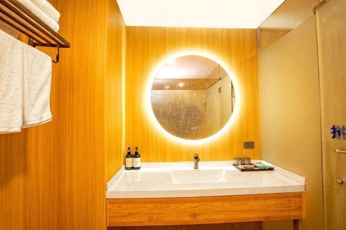 A bathroom with wooden paneling, a round mirror with a light, and a white sink.