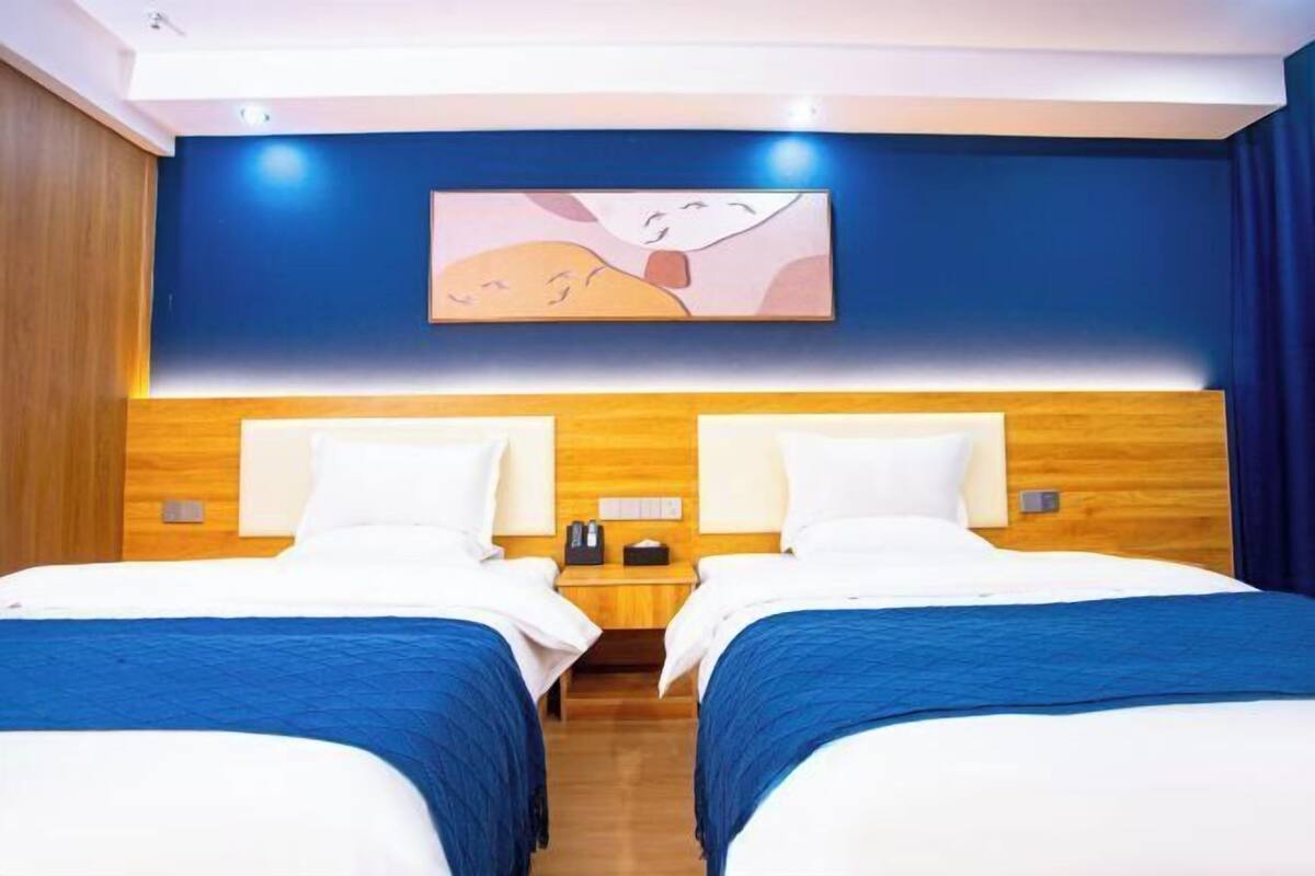 Ein Hotelzimmer mit zwei Betten, einem Holzkopfstück, einem Nachttisch mit Lampe und einem Gemälde an der Wand.