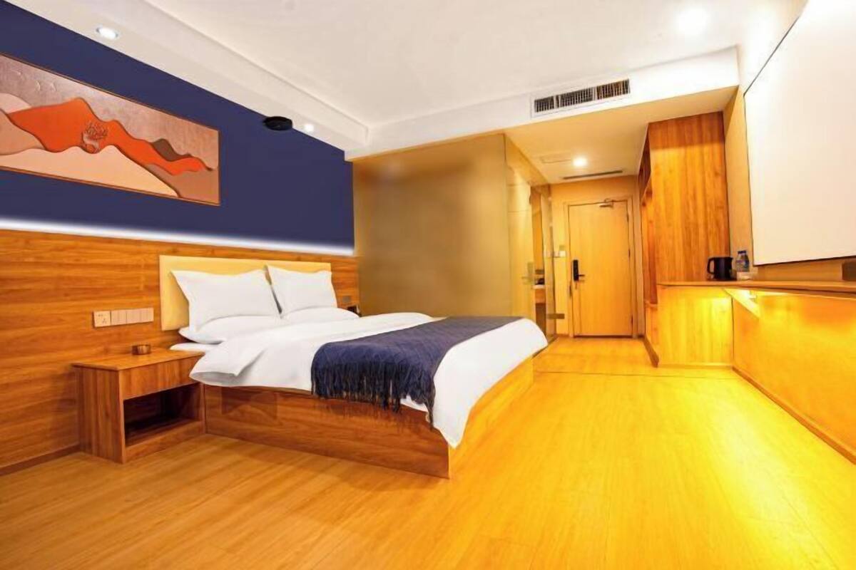 Ein Hotelzimmer mit einem hölzernen Bett, einem Nachttisch, einem Bild an der Wand und einer Küchenzeile mit Holzschränken.
