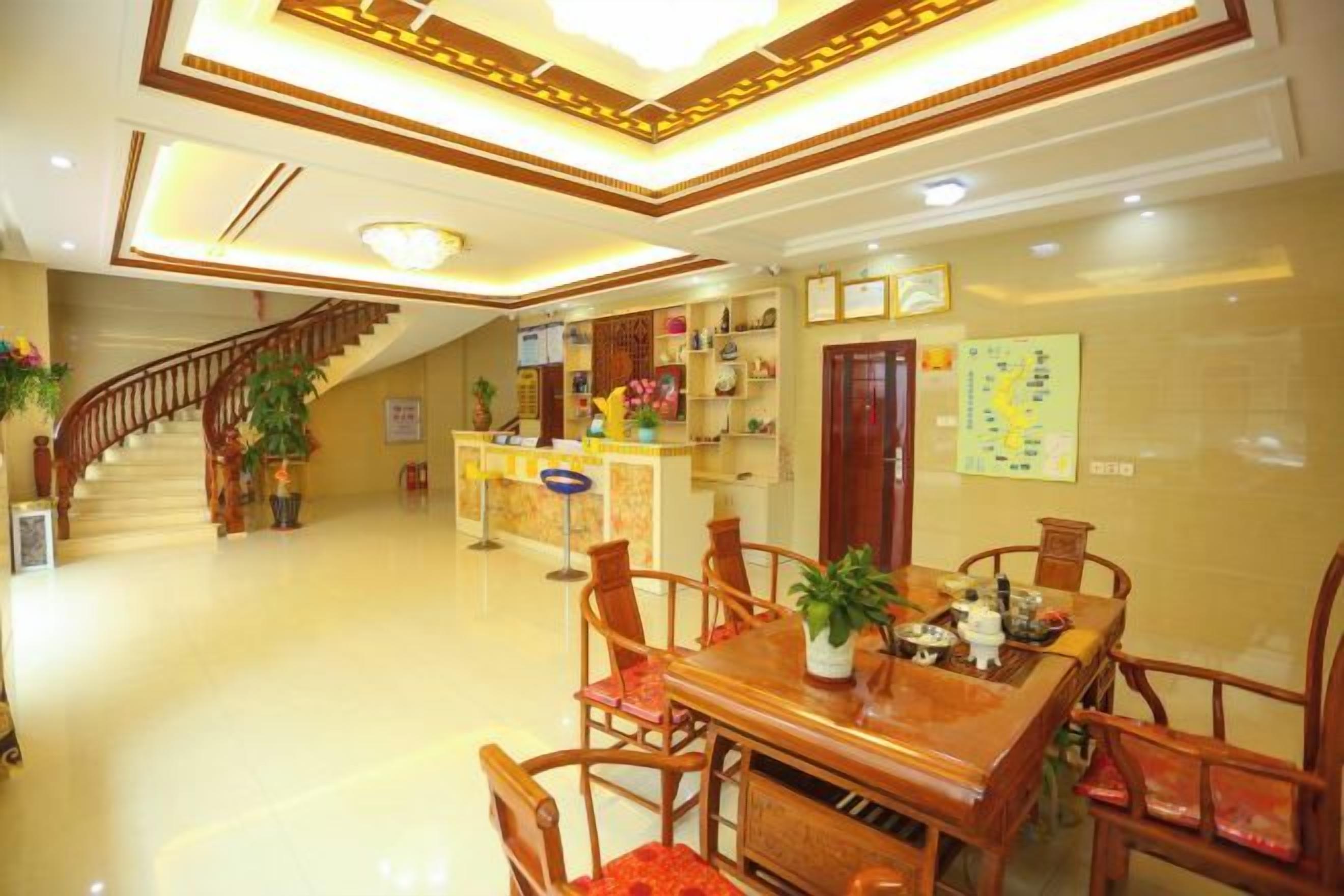 A hotel lobby with a reception desk, a staircase, and a dining area with wooden furniture.
