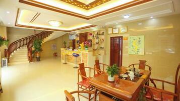 A hotel lobby with a reception desk, a staircase, and a dining area with wooden furniture.