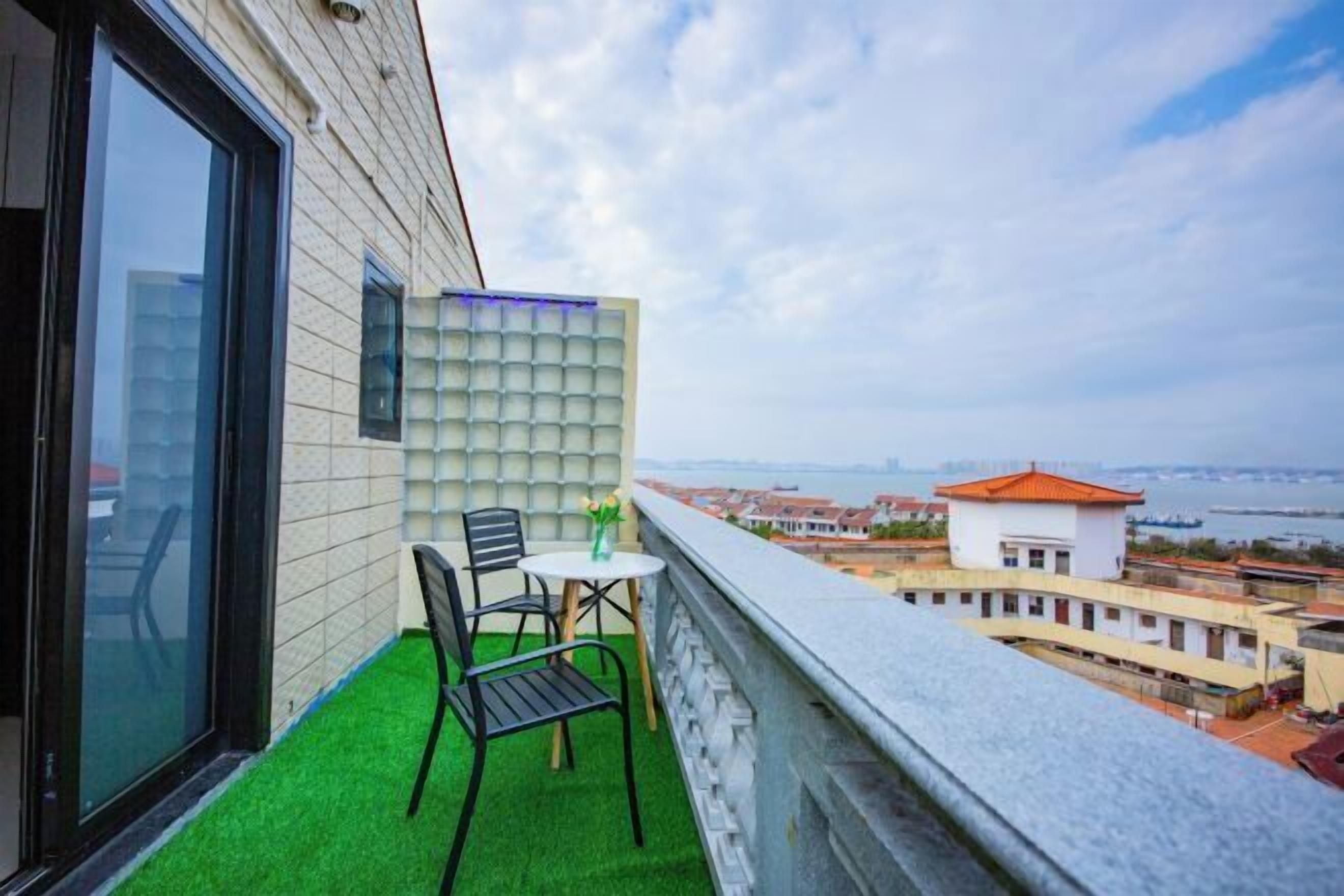A balcony with artificial green turf, a table with chairs, and a view of a cityscape and water.
