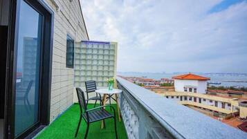 A balcony with artificial green turf, a table with chairs, and a view of a cityscape and water.