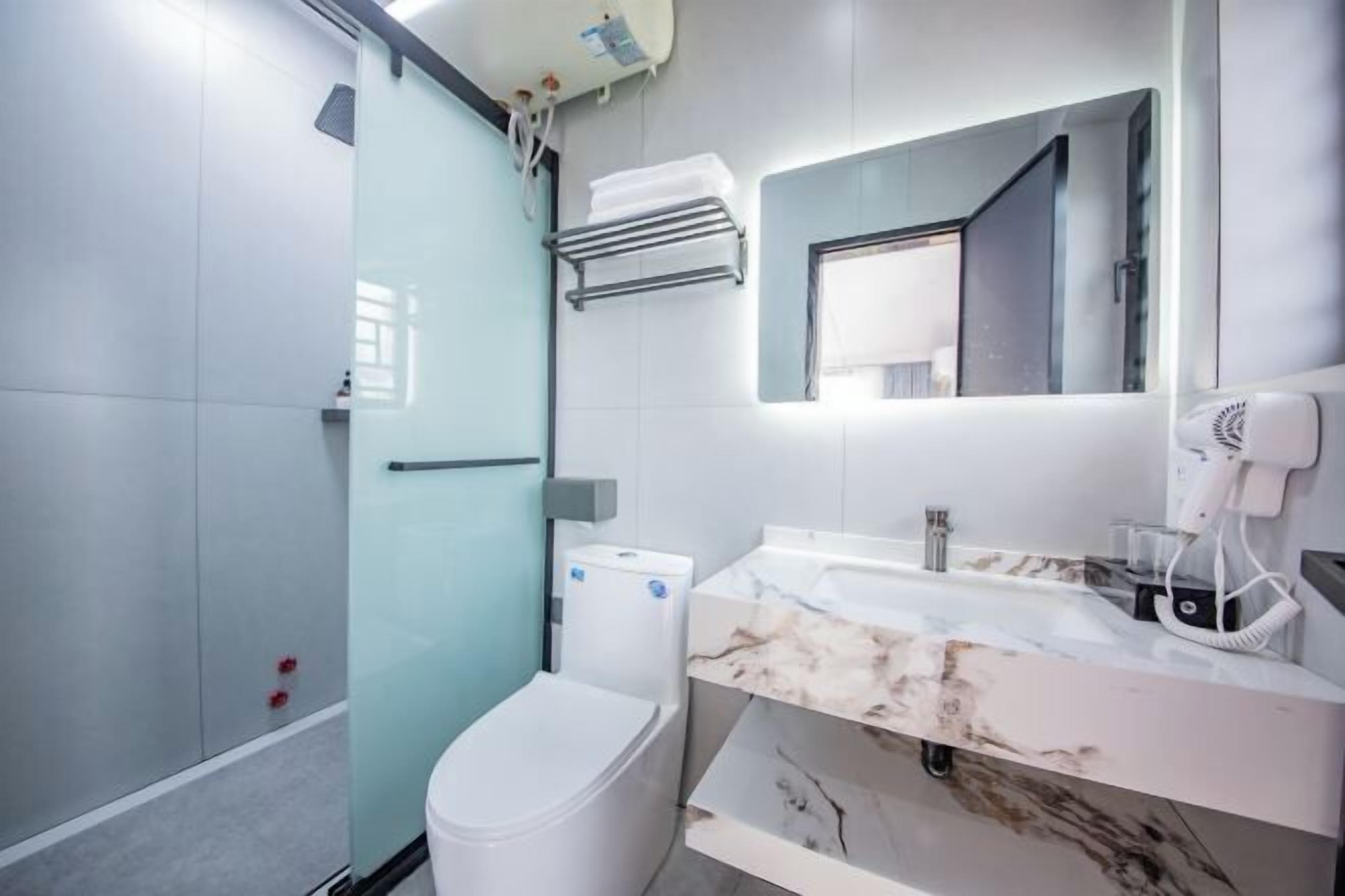 A modern bathroom with a glass shower enclosure, a white toilet, a marble sink, and a hairdryer on the countertop.