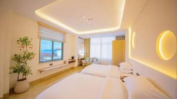 A modern hotel room with a large bed, bedside tables, a potted plant, and a view of the cityscape.