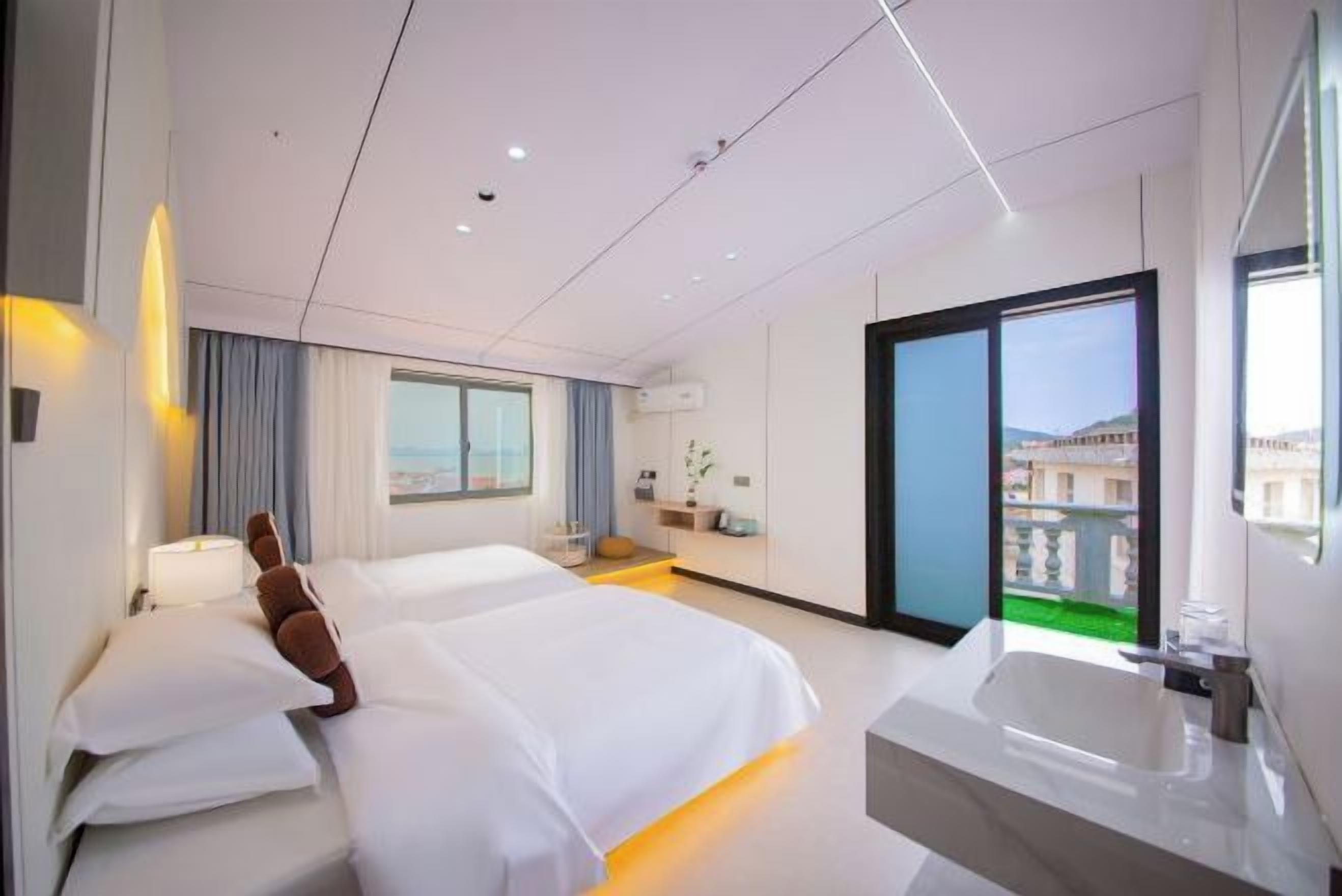 A modern hotel room with two beds, a large window, a balcony, and a separate bathroom with a bathtub.