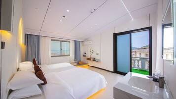 A modern hotel room with two beds, a large window, a balcony, and a separate bathroom with a bathtub.