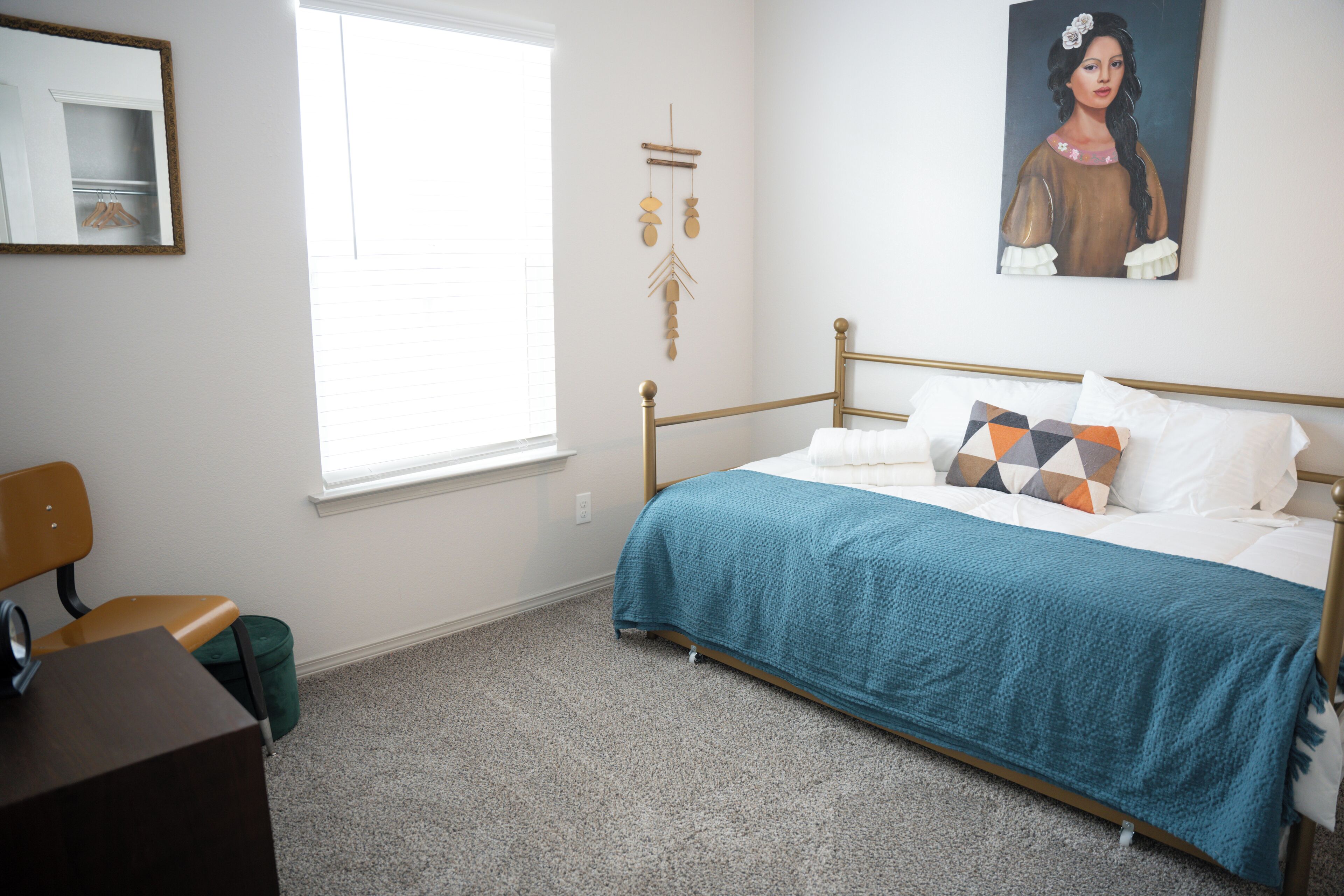 A bedroom with a bed, a chair, a desk, a window, and a wall decoration.