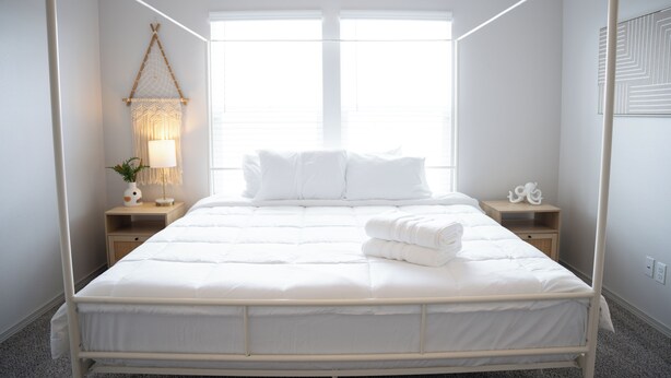 Ein ordentlich gemachtes Bett mit weißer Bettwäsche, einer Nachttischlampe und einem Wanddekor.