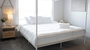 Ein Himmelbett mit weißer Bettwäsche, eine Nachttischlampe und ein an der Wand befestigtes abstraktes Kunstwerk.