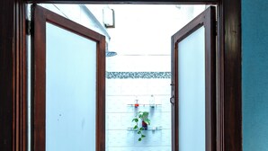 Een open houten deur die leidt naar een betegeld terras met een bloempot.
