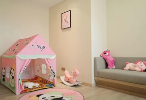 A children's play area with a pink tent, a rocking horse, and plush toys on a sofa.