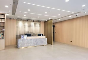 A reception area with a marble counter, a security camera, and a wooden panel wall. - Joyful Star Hotel (Shanghai)
