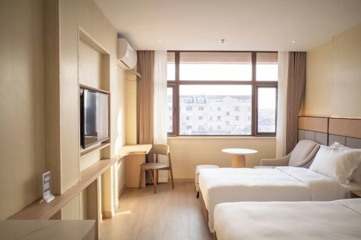 Hotelkamer met twee bedden, een bureau, een stoel, een televisie en een raam met uitzicht op de stad.