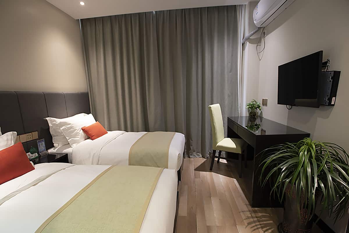 Hotelkamer met twee bedden, een bureau, een stoel, een televisie en een kamerplant.