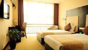 Una habitación de hotel con dos camas, un escritorio, una silla, una planta en maceta y un ventanal grande.