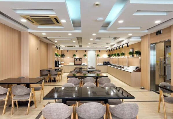 A modern hotel dining area with multiple tables and chairs, a kitchen counter, and a refrigerator. - Joyful Star Hotel (Shanghai)