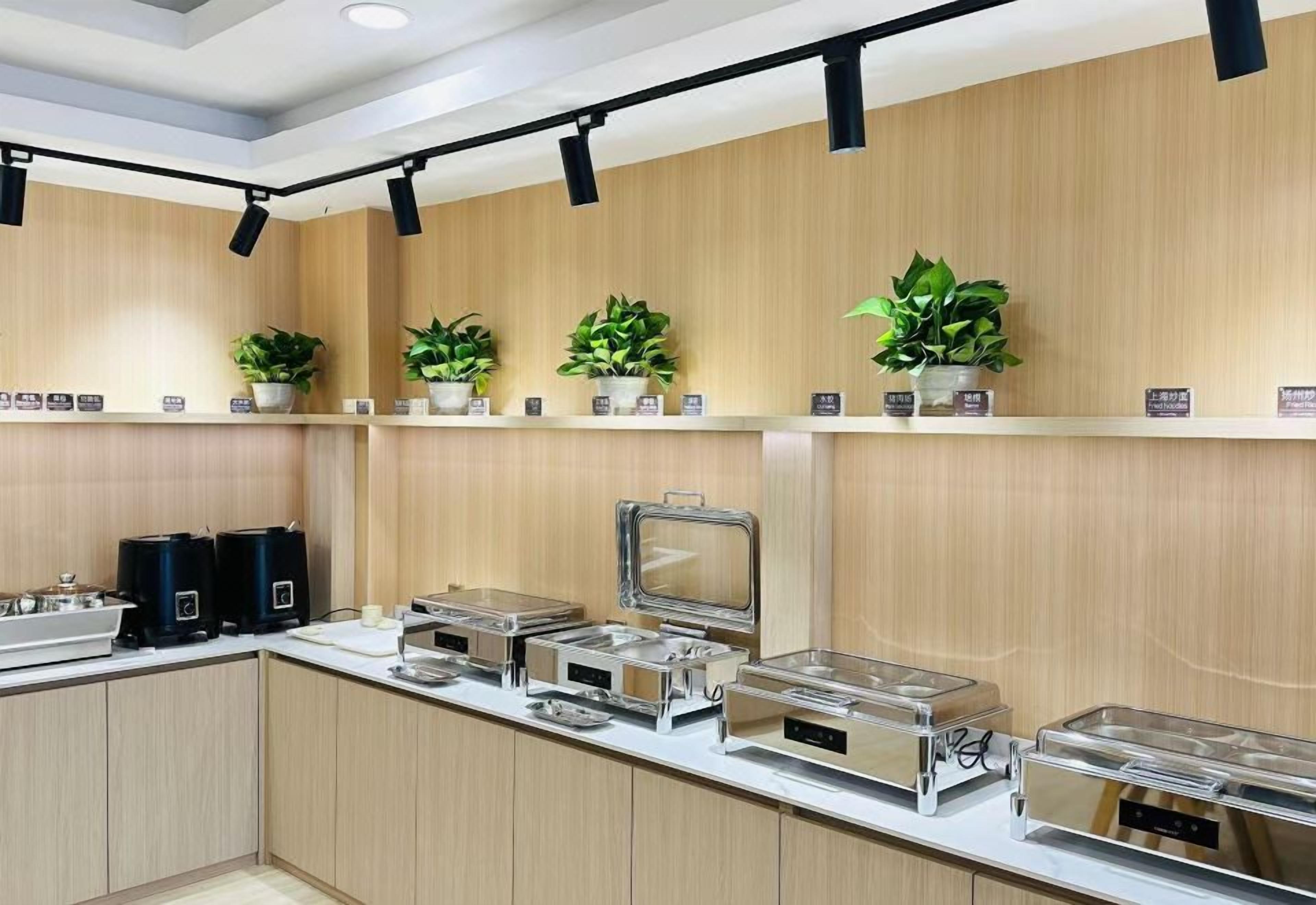 A buffet setup with multiple serving stations, potted plants, and overhead lighting.