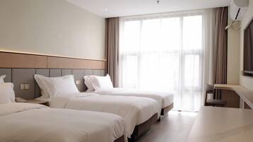 A hotel room with two beds, a desk, and a large window with curtains.