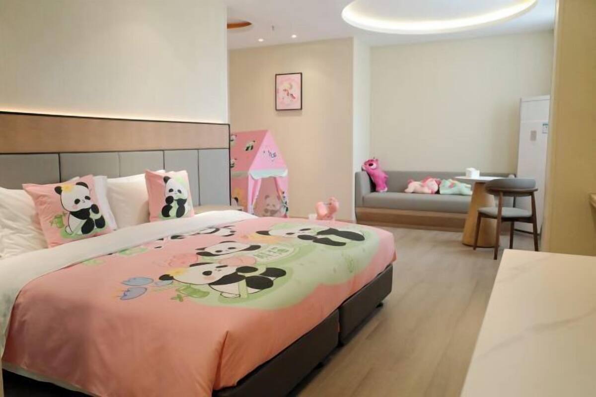 Een hotelkamer met een bed met een stripfiguurprint, een klein tafeltje, een stoel en een bank.