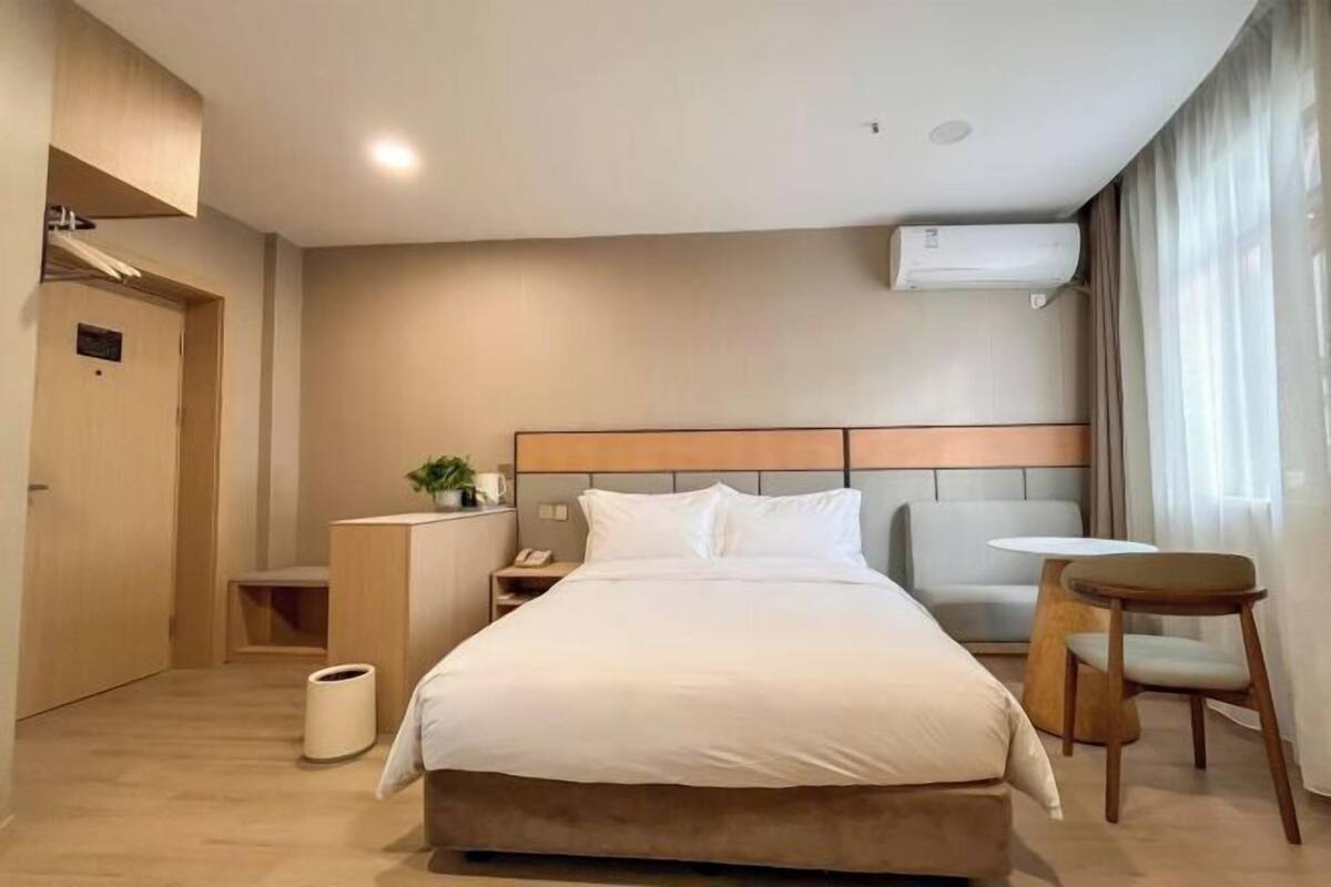 Een moderne hotelkamer met een groot bed, een nachtkastje, een stoel, een kleine tafel en een airconditioner.