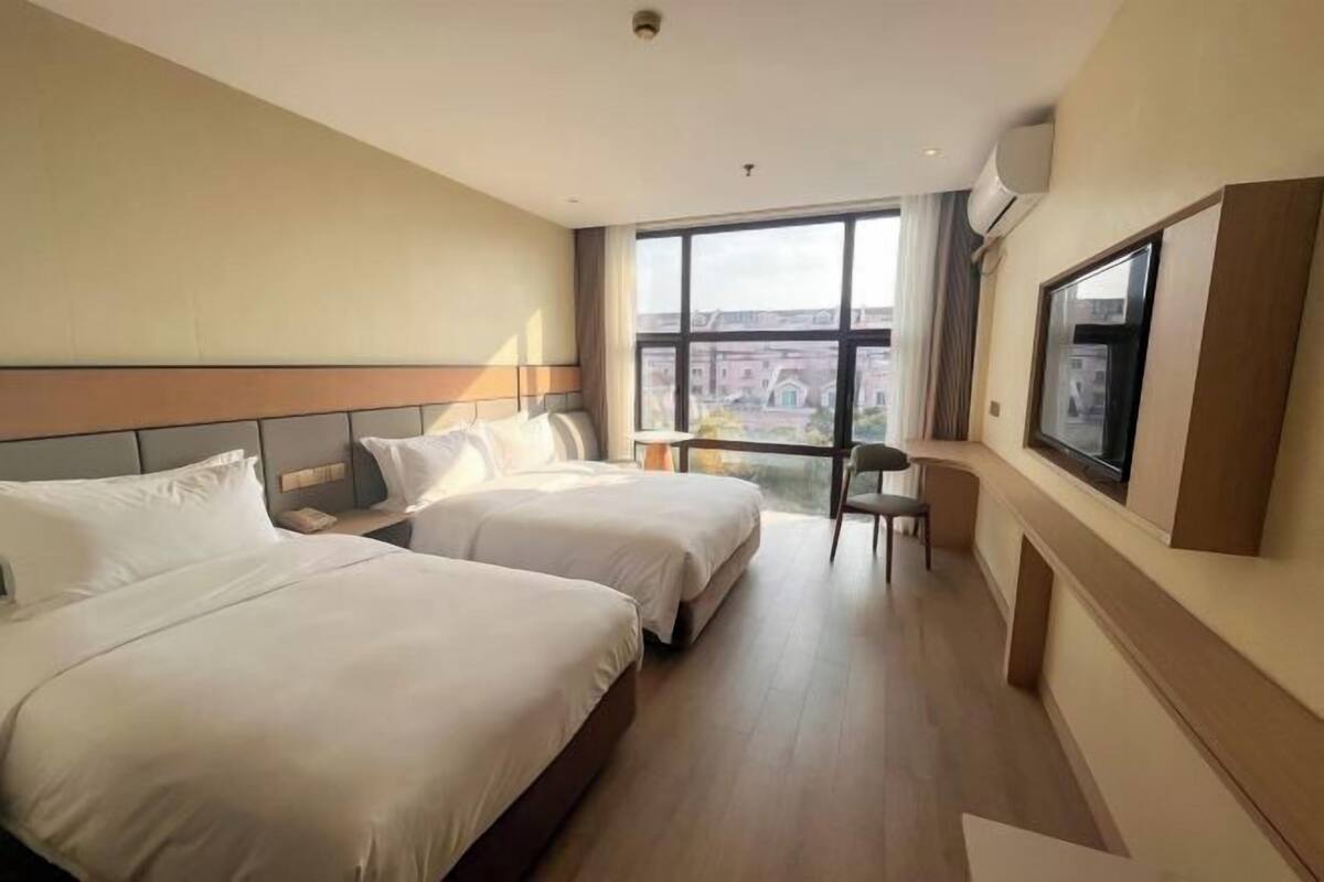 Een hotelkamer met twee bedden, een bureau, een stoel, een groot raam met uitzicht en een airconditioning.