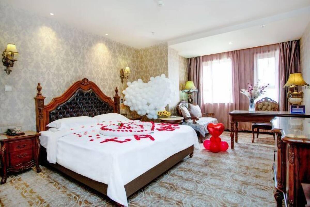 A hotel room with a large bed, a desk, and a chair. There are decorative items on the bed and a large white balloon decoration.
