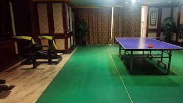 A room with a green carpet, a ping pong table, exercise equipment, and a door with curtains.