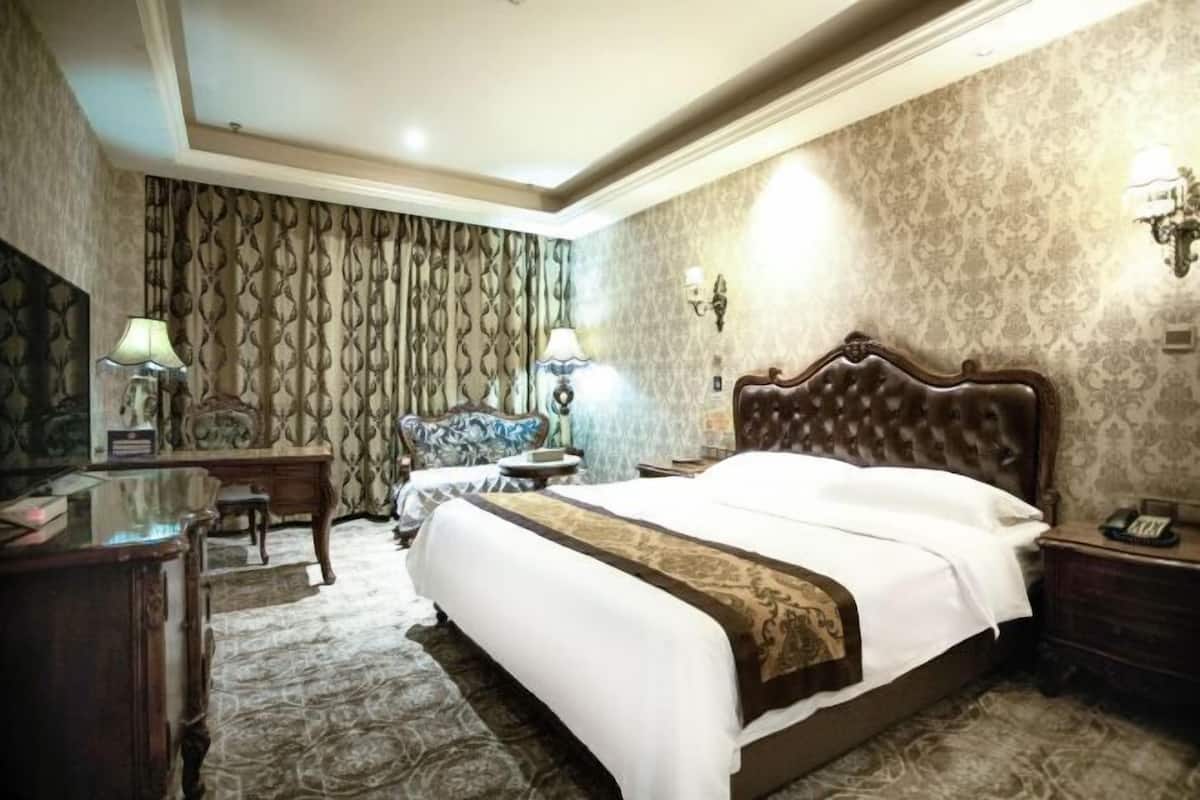 A hotel room with a large bed, a desk, a chair, and a lamp.