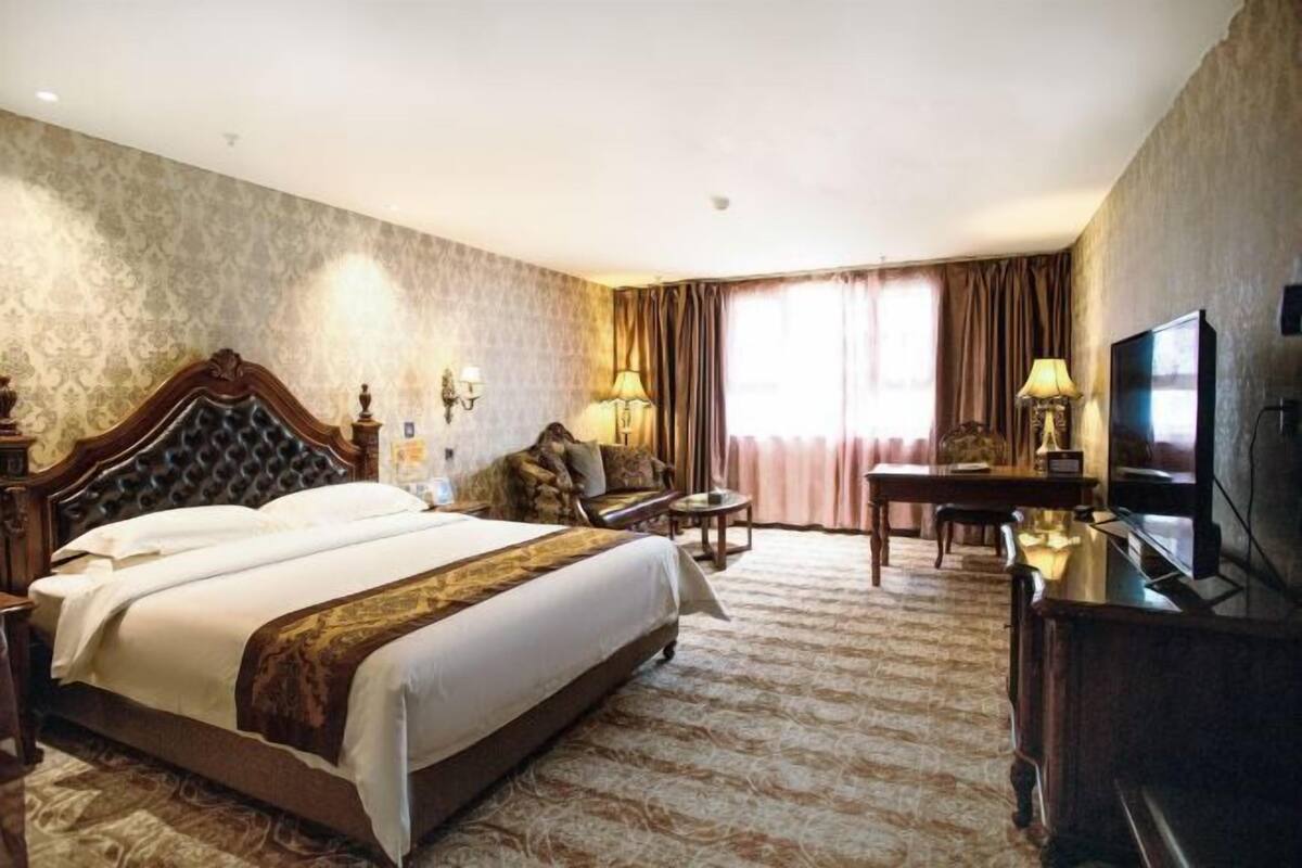 A hotel room with a large bed, a desk, a chair, a television, and a lamp.