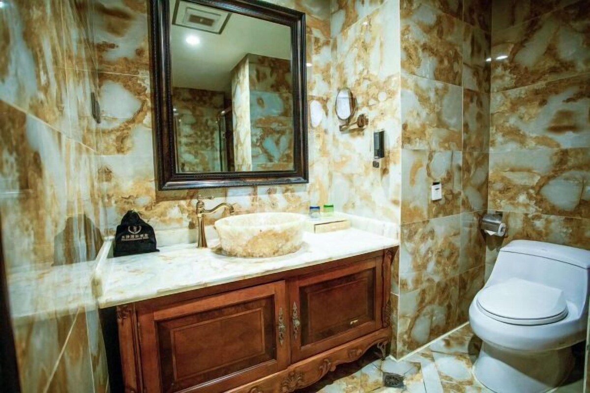 A bathroom with marble walls, a wooden vanity, a round sink, and a toilet.