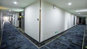 A long, narrow hotel corridor with a carpeted floor, white walls, and a central column. - Tianjin International Hotel (Hotan City)