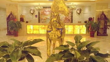 Un vestíbulo con una estatua de un caballo dorado, una recepción y plantas en macetas.