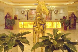 Un vestíbulo con una estatua de un caballo dorado, una recepción y plantas en macetas.