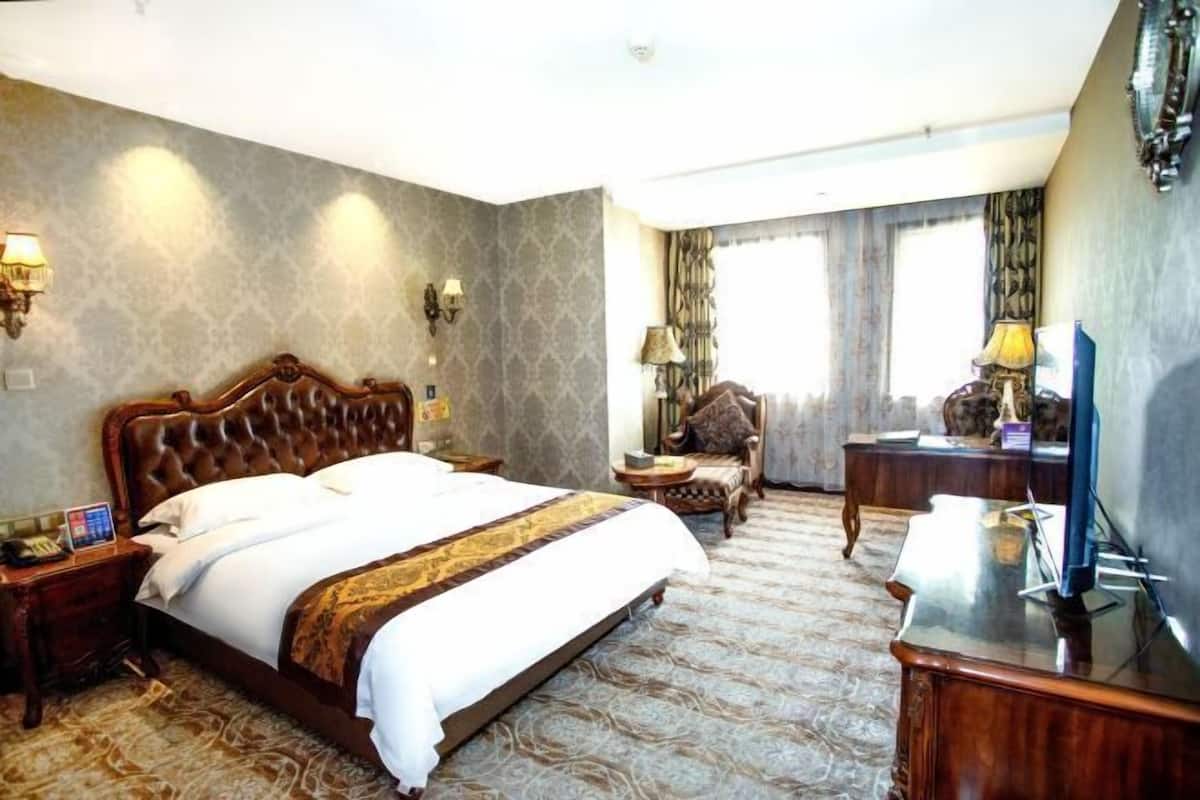 A hotel room with a large bed, a desk, a chair, a TV, and two lamps.