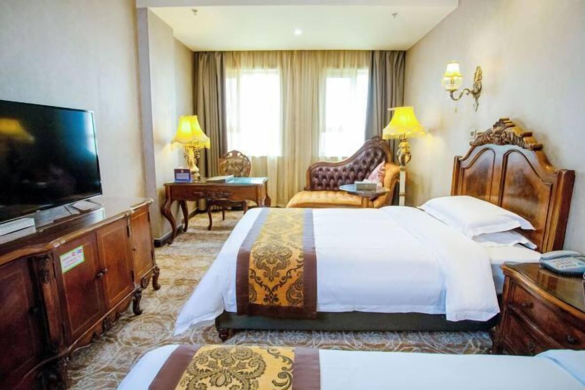 A hotel room with a bed, a television, a desk, and two lamps.
