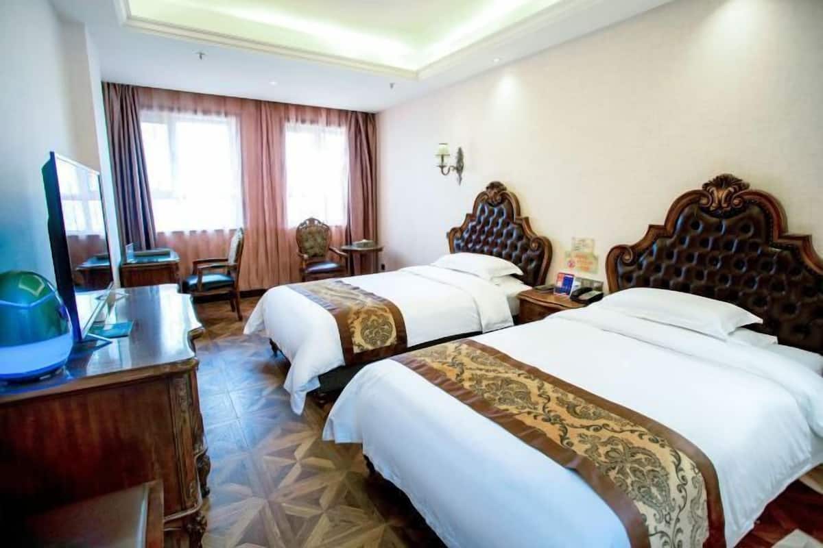 A hotel room with two beds, a desk with a computer, a chair, and a television.