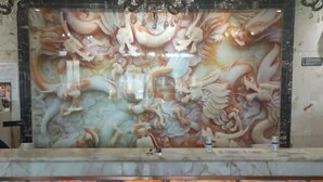 Un comptoir d’accueil avec un plan de travail en marbre et, en arrière-plan, une grande fresque décorative.