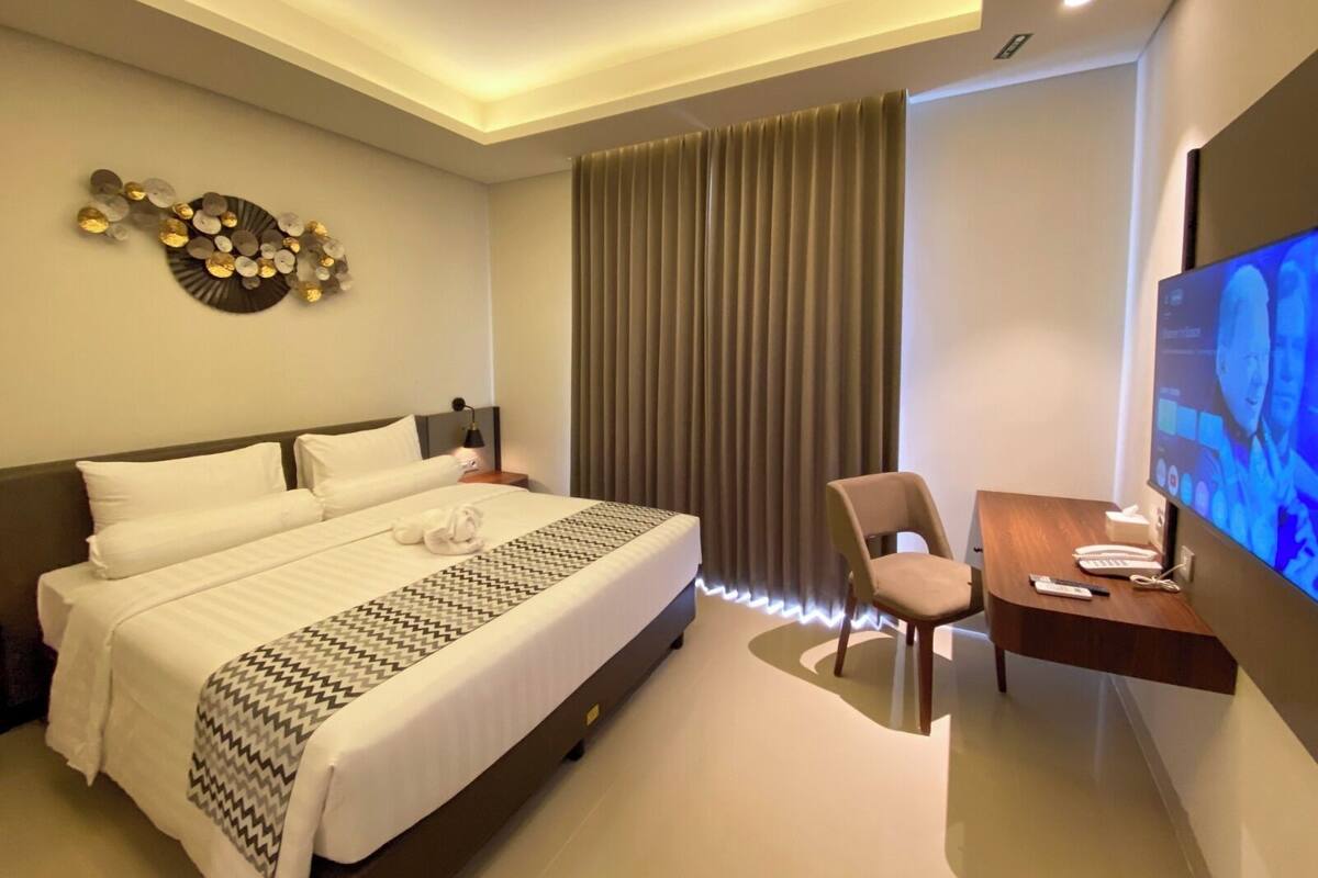 Habitación de hotel con cama, escritorio con silla, televisor y un adorno en la pared.