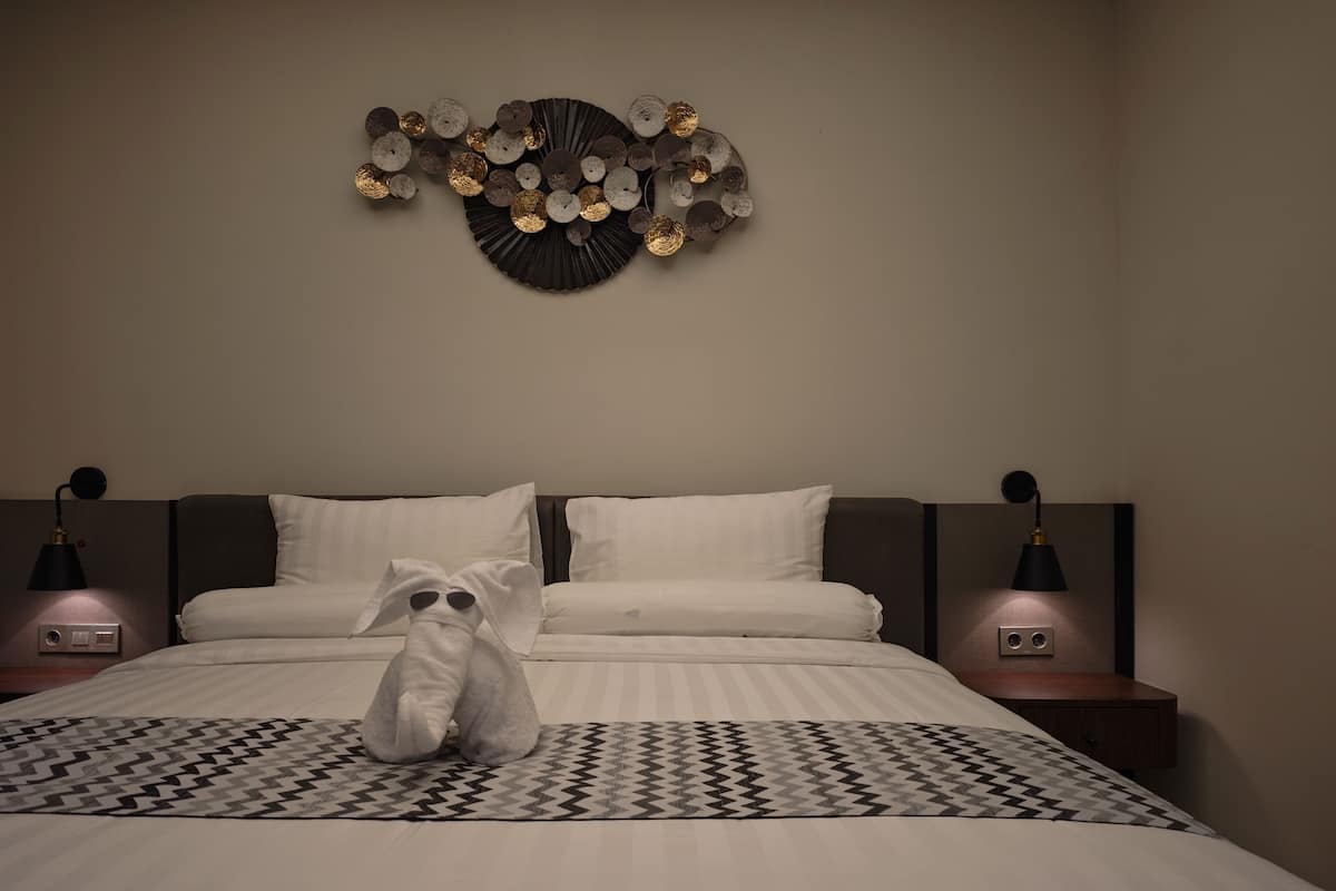 Una cama bien hecha con una colcha estampada, dos lámparas de noche y una decoración en la pared sobre la cama.