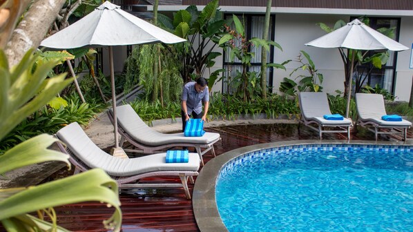 A poolside area with lounge chairs and umbrellas, a man carrying a blue towel, and a building in the background. - Azana Garden Hill Resort Blora (Blora)