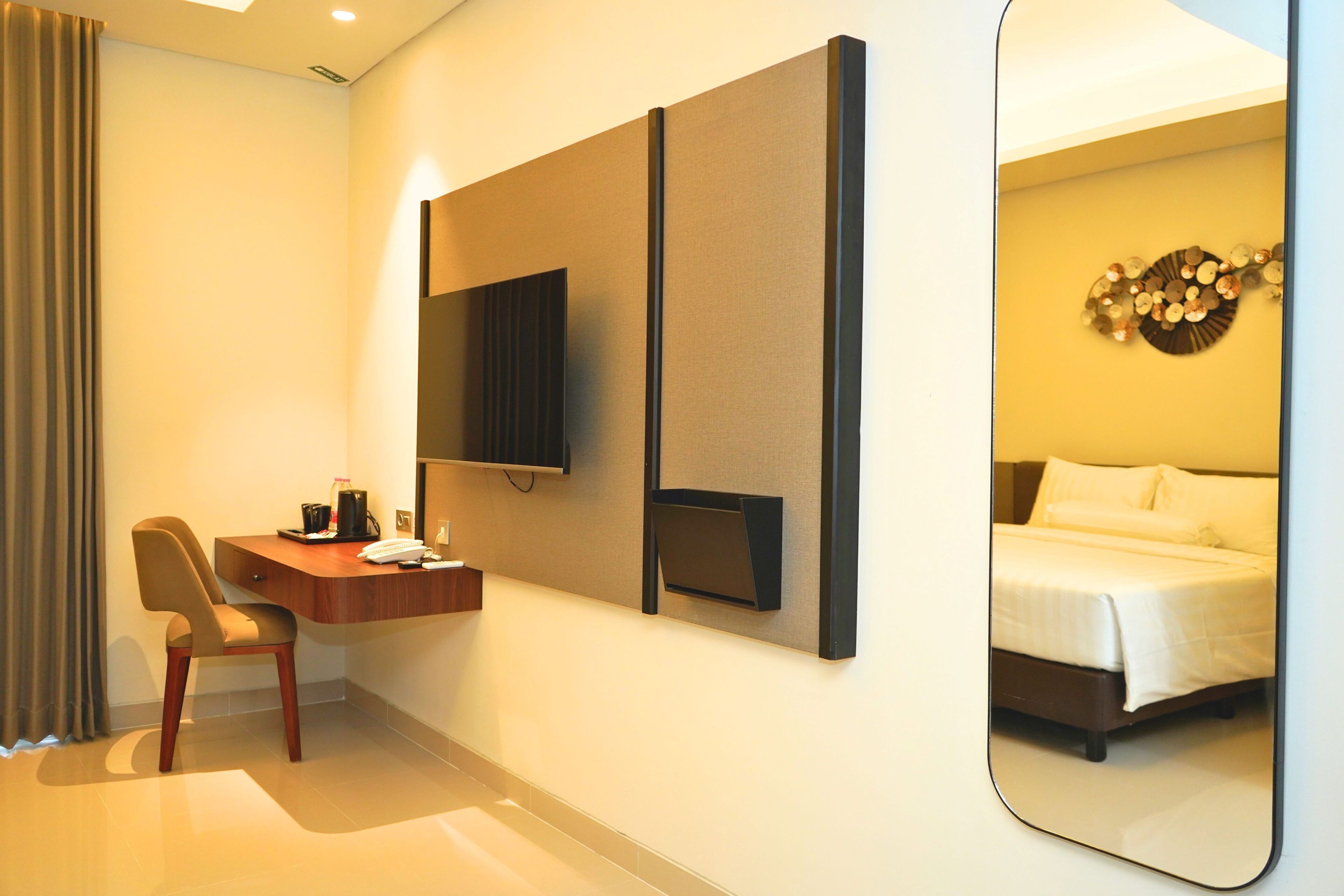 Habitación de hotel con escritorio, silla, cama y un espejo grande.