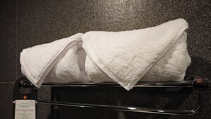 Una toalla blanca doblada sobre un perchero metálico en un baño con pared de azulejos oscuros.