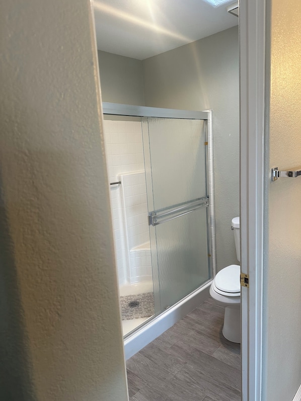 Une salle de bain avec une douche à parois de verre, des toilettes et un carrelage au sol.