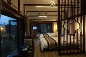 Une chambre d’hôtel avec deux lits, une télévision, une cloison en bois et une fenêtre avec des rideaux.