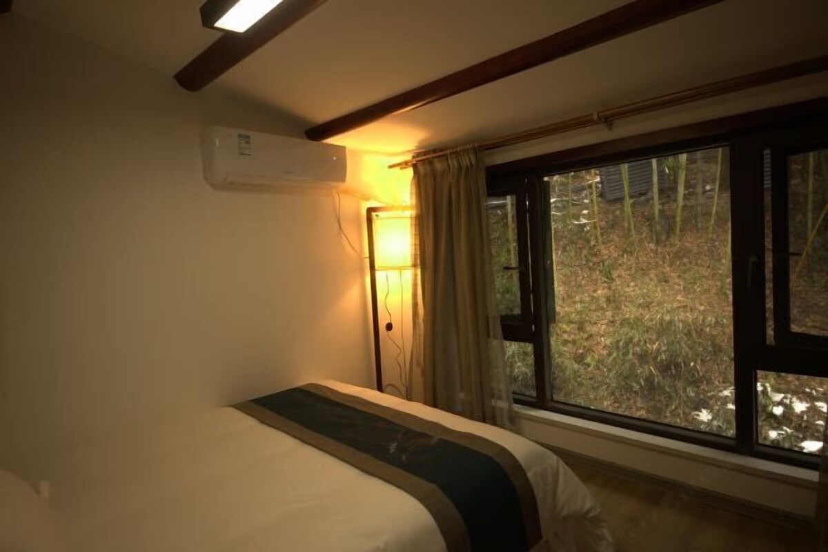 Une chambre à coucher comprenant un lit, un appareil de climatisation, une fenêtre avec des rideaux et une vue sur l’extérieur.