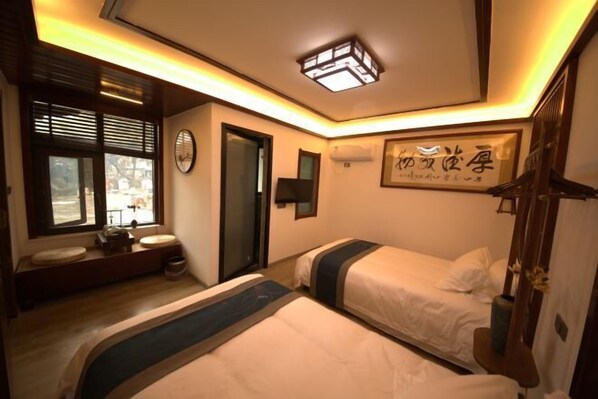 Une chambre d’hôtel avec deux lits, une fenêtre avec des stores, une table de chevet, une horloge murale et un luminaire au plafond.