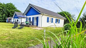Uma casa de dois andares com fachada azul e detalhes brancos, um gramado e um deck de madeira.